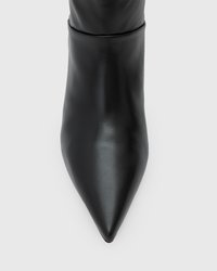 Stivale alla caviglia in pelle nera con punta appuntita, caratterizzato da una texture liscia e un design con risvolto aderente. Colore uniforme senza motivi o accenti.