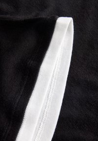 Črn material z gladko teksturo, obdan z belim rebrastim robom. Oblika je preprosta in vključuje urejene šiviljske podrobnosti.