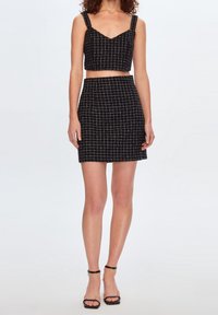 Ensemble bi-matière noir à carreaux comprenant un top court à larges bretelles et une jupe ajustée. Le matériau a une finition texturée. Accentué par un motif à grille.