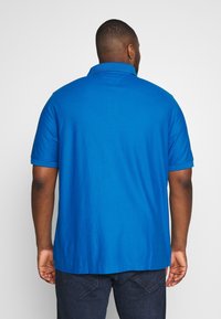 Blå kortärmad polo skjorta med en enkel krage, tillverkad av ett slätt tyg. Baksidan visar jämn sömnad och en rak kant.