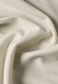 Tissu beige clair avec un tissage texturé, affichant de douces plis et de subtiles variations de surface pour une apparence confortable.