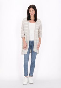 Cardigan beige chiaro con righe orizzontali bianche, design aperto sul fronte, maniche a tre quarti, abbinato a una maglietta bianca aderente e jeans blu.