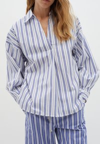 Camicia a righe bianca e blu, con maniche lunghe, colletto e vestibilità morbida. Abbinata a pantaloni a righe coordinati.