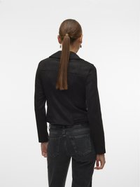 Zwarte suède jas met een getailleerd ontwerp, lange mouwen en een licht cropped pasvorm, gecombineerd met donkerblauwe, hooglopende jeans.