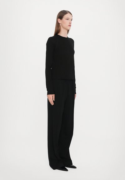 Svart langermet topp med rund hals, kombinert med løse svarte bukser. Antrekket har en jevn tekstur og minimalistisk design.