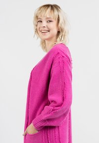 Różowy, oversize sweter z teksturowanym splotem, z opadającymi ramionami, długimi rękawami i bocznymi kieszeniami. Zniszczone detale wzdłuż szwów.