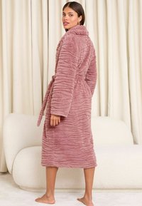 Accappatoio morbido e rosa, peloso, con un motivo testurizzato e ondulato. Presenta un colletto sciallato e una cintura abbinata. Design fino al polpaccio.