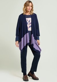 Marineblauwe en lavendelkleurige kleurblokkade cardigan met gedrapeerd ontwerp, gemaakt van zachte stof. Draag over een bedrukt topje en gecombineerd met donkere broek en schoenen.