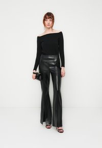Top nero off-the-shoulder abbinato a pantaloni in pelle nera a vita alta e svasati. Design aderente con texture liscia e leggero luccichio.