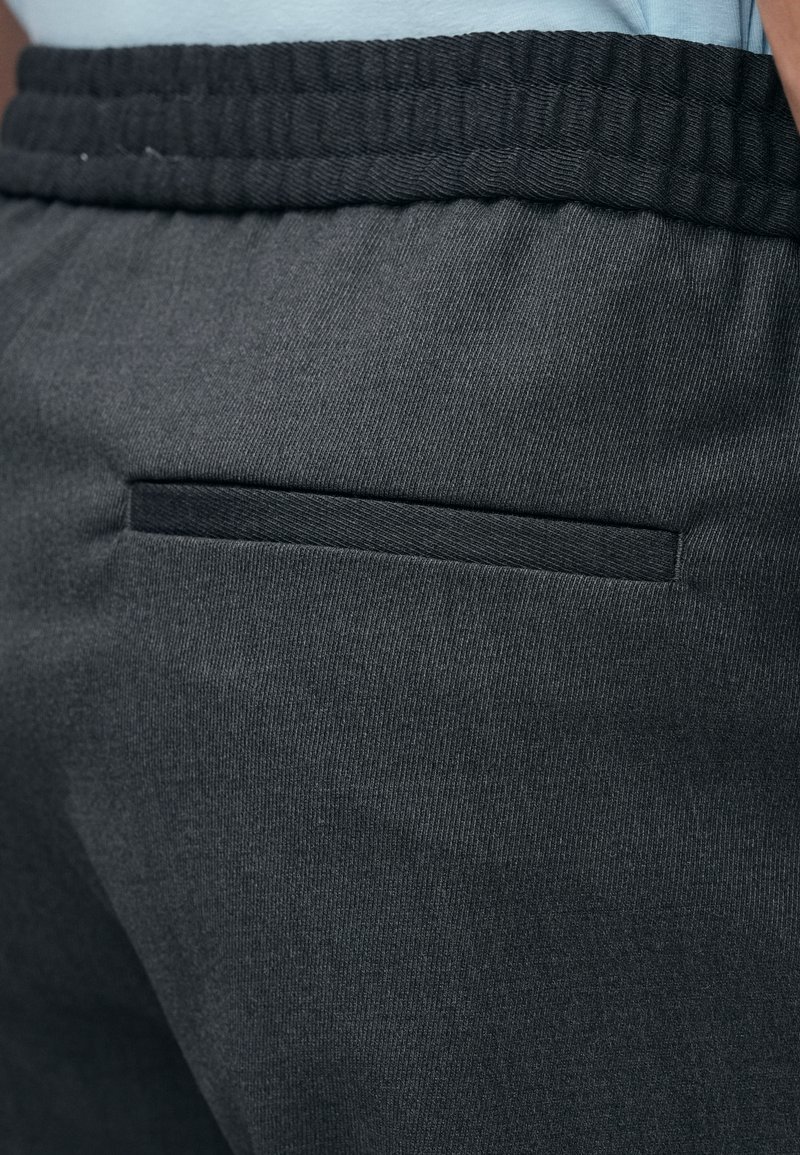 Schwarze, zulaufende Hose mit glatter Textur, ausgestattet mit einer einzigen Gesäßtasche und einem elastischen Bund für Komfort und Trageleichteit.