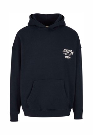 Donker marineblauwe hoodie met een voorste kangoeroezak. Heeft witte tekstbranding aan de bovenkant links. Gemaakt van katoen.