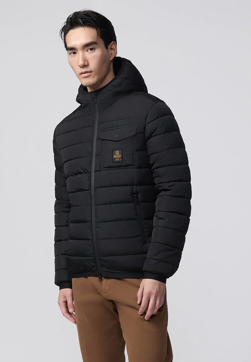 Giubbotto imbottito nero con cappuccio, dotato di sezioni quilted orizzontali, una tasca sul petto con patta a pressione e polsini neri.