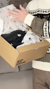 Persona rakstā džemperī tur atvērtu kastīti ar North Face jaku un zīmola iesaiņojuma papīru iekšpusē.