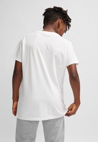 Hvid bomulds t-shirt med korte ærmer, en afslappet pasform og en rund halsudskæring. Ryggen vises, hvilket fremhæver den glatte tekstur og søm.
