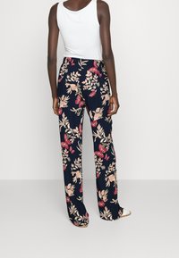 Blommönstrade vida byxor i marinblått med rosa och krämfärgade blommor och fjärilar; lätt tyge; ihop med en vit linne.