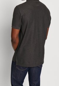 Polo gris charbon à manches courtes, avec un col, de légères fentes latérales et une texture lisse, associé à un jean bleu foncé.