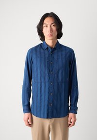 Cămașă din denim, albastru închis, cu dungi verticale, două buzunare pe piept și nasturi maro. Prezintă manșete cu nasturi și guler simplu.
