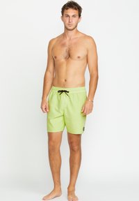 Pantaloncini da bagno verde lime con cintura elastica, cordino nero e patch con logo sulla gamba sinistra. Tessuto liscio e lunghezza fino a metà coscia.