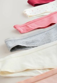 Diverse dameskatoenen ondergoed in grijs, roze, crème, wit met stippen en donkerozen, plat gelegd op een neutrale ondergrond.