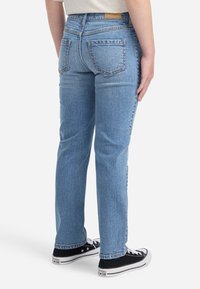 Svijetloplave traperice sa ravnim krojem. Imaju stražnje džepove i srednje visoki struk. Uparene su s crnim tenisicama niske pete.