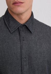 Schwarzes Denim-Hemd mit einem strukturierten Kragen, Knopfleiste, sichtbarer Textur und dezenten diagonalen Streifen im Stoffmuster.