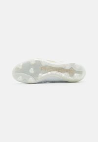 Suela de zapatilla de fútbol blanca con un patrón texturizado, que presenta una parte inferior de goma transparente y la marca en dorado "PREDATOR".