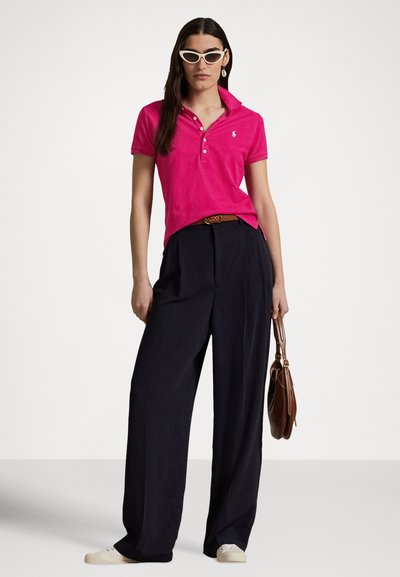 Ροζ φούξια πόλο πουκάμισο με γιακά και τρεις κουμπότρυπες, σε συνδυασμό με φαρδιά σκούρα μπλε παντελόνια. Αξεσουάρ περιλαμβάνουν καφέ ζώνη και τσάντα χειρός.