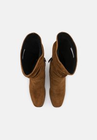 Brown suede ankle boots with a slouchy design. Features a soft black lining and a side zipper for closure. Smooth texture and tapered toe.