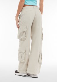 Beige cargo-bukser med løs pasform, flere sidelommer, enkel syning og en glat tekstur. Kombinationen med sorte og hvide sneakers.