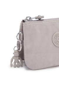 Grijze stoffen pouch met een gestructureerd oppervlak, zilveren rits en een sleutelhanger met een kleine grijze figuur. Circulair logo in reliëf op de voorkant.