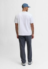 Bílý tričko s krátkým rukávem a šedé kalhoty viděné zezadu; modrá kšiltovka, volnočasové tenisky; hladká tkanina, uvolněný střih a styl.