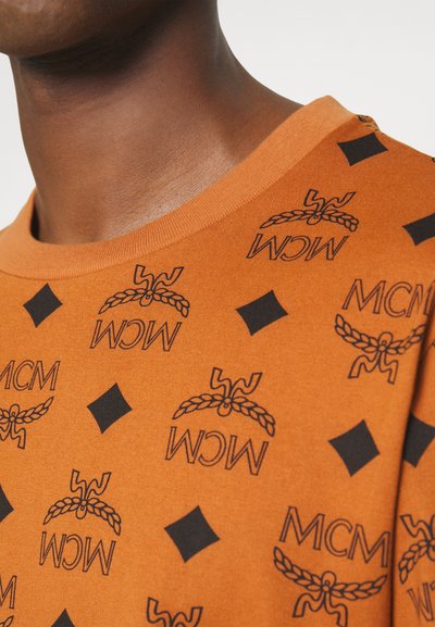 Orange bomullströja med svart MCM-logotyp och diamantmönster. Rundad halsringning med en mjuk struktur och minimal sömdetalj.