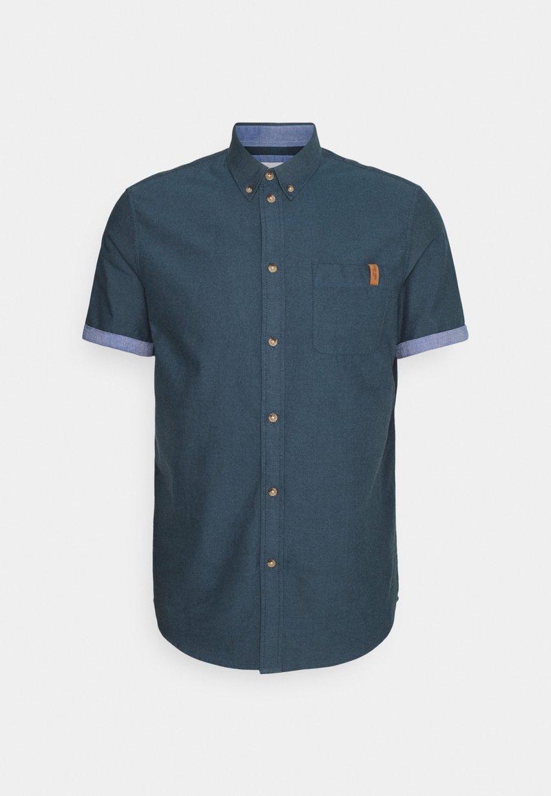 Chemise homme bleu foncé à manches courtes avec boutons, manches intérieures bleu clair contrastantes, col boutonné et poche poitrine avec étiquette beige.