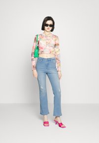 Top colorido de manga longa cropped com vários padrões, combinado com jeans claros rasgados azuis e sandálias de salto alto rosas choque com tiras. Bolsa verde.