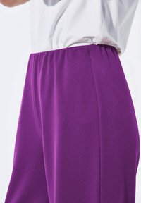 Pantalons violets en tissu doux et extensible. Comprennent une taille élastique et une texture lisse avec un design à jambes droites.