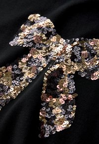 Schwarzer Stoff mit einem Schleifendessin, das aus kleinen, glänzenden Pailletten in Gold, Bronze und Schwarz besteht.