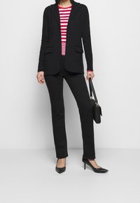 Czarny żakiet z klapami, przednimi kieszeniami i trzema guzikami, w połączeniu z czerwoną i białą w paski koszulą oraz czarnymi spodniami, stylizowany z czarnymi szpilkami.