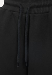 Černé tepláky s vroubkovaným pasem a šňůrkou s plastovými koncovkami, vyrobené z měkké tkaniny s hladkým povrchem.