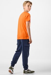 Orange kortærmet t-shirt parret med marineblå cargo bukser med sidelommer og grønne sko med hvide detaljer. Simpelt, afslappet design.