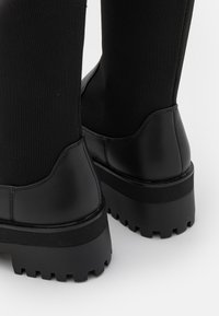 Botines negros con una parte superior de tela texturizada y un tacón de cuero suave. Suelas gruesas y robustas que ofrecen tracción y estabilidad.