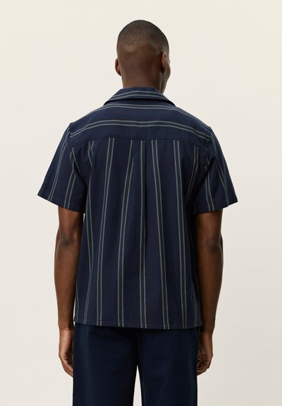 Chemise à manches courtes bleu marine avec rayures verticales. Dotée d'un col plat et d'un empiècement dos. Confectionnée en tissu léger au toucher lisse.