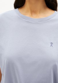 Světle fialové bavlněné tričko s kulatým výstřihem a kr�átkými rukávy, které má na levé straně hrudi malé vyšívané kulaté logo.