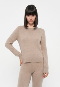 Beige strikket genser med rund hals og lange ermer, med ribbestrikkede mansjetter og nederkant, laget av myk, teksturert stoff.
