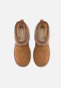 Botas de tobillo de ante marrón con un suave forro en tonos marrón claro y costuras decorativas a lo largo del cuello. Superficie exterior texturizada, diseño sencillo.