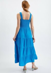 Blå, lager-på-lager maxi klänning med smockad byst, breda axelband och mjukt tyg. Har en flödande silhuett och ojämn fåll.