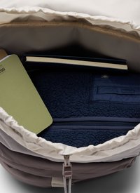 Open bag showing a navy fleece jacket, a closed book with cream pages, and a partially visible green notebook inside.