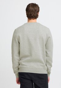 Sudadera gris claro con cuello redondo, hecha de tela suave. Presenta puños y dobladillo acanalados, con un diseño liso y sencillo.