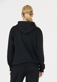 Felpa nera con cappuccio, dal taglio rilassato, con polsini e vita a coste. Texture morbida, design minimal senza loghi o fantasie.