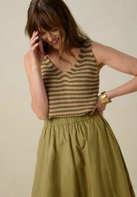 Haut en tricot rayé rose et vert, avec un col en V et sans manches. Associé à une jupe taille haute olive avec une ceinture élastique.