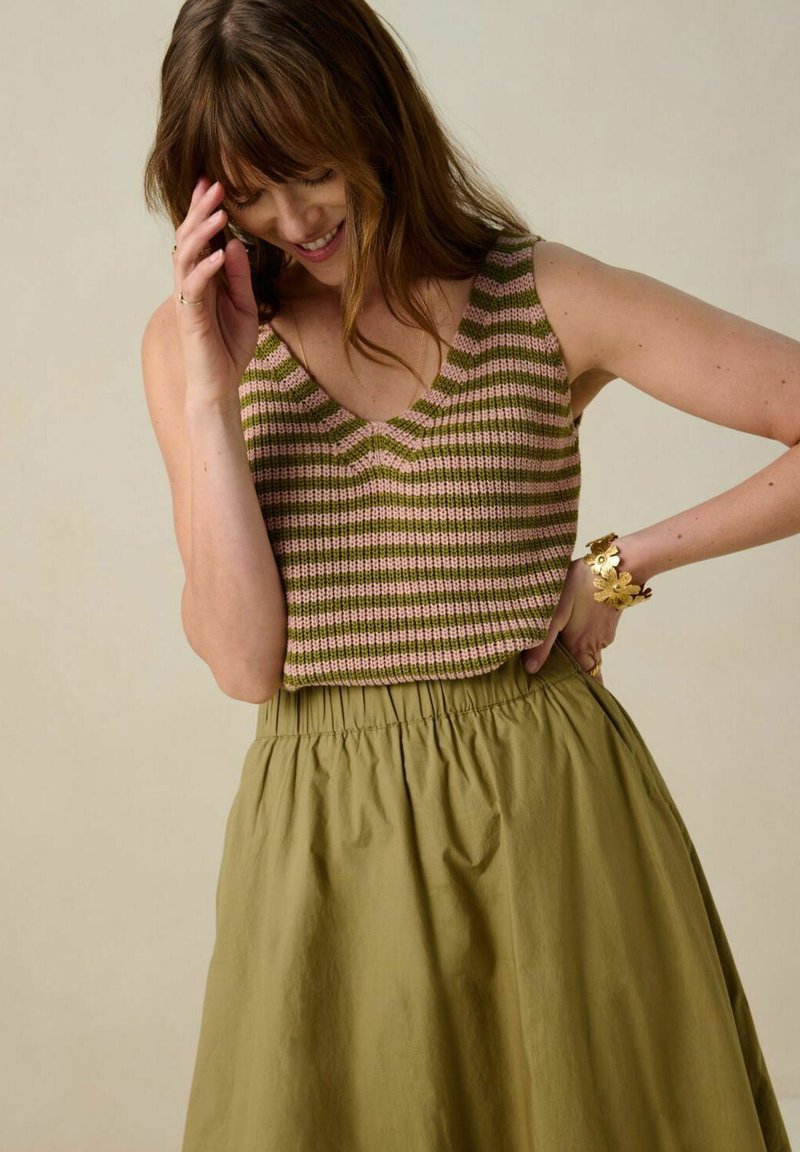 Haut en tricot rayé rose et vert, avec un col en V et sans manches. Associé à une jupe taille haute olive avec une ceinture élastique.
